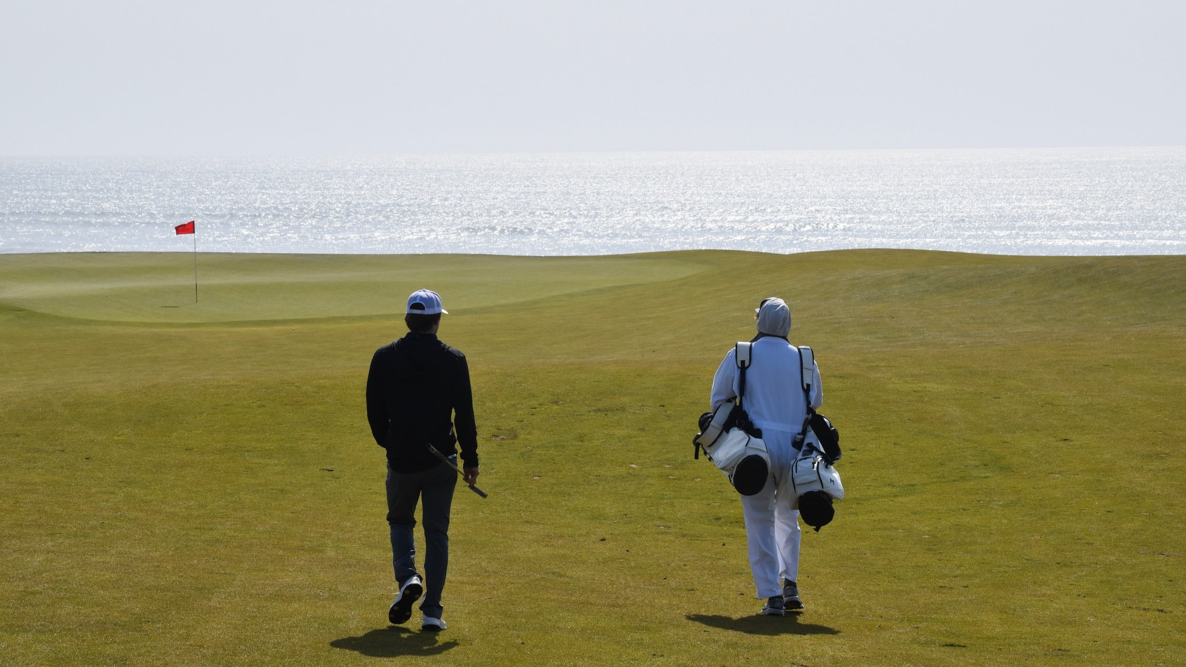 two mnml golf bags at beautiful course with ocean in background