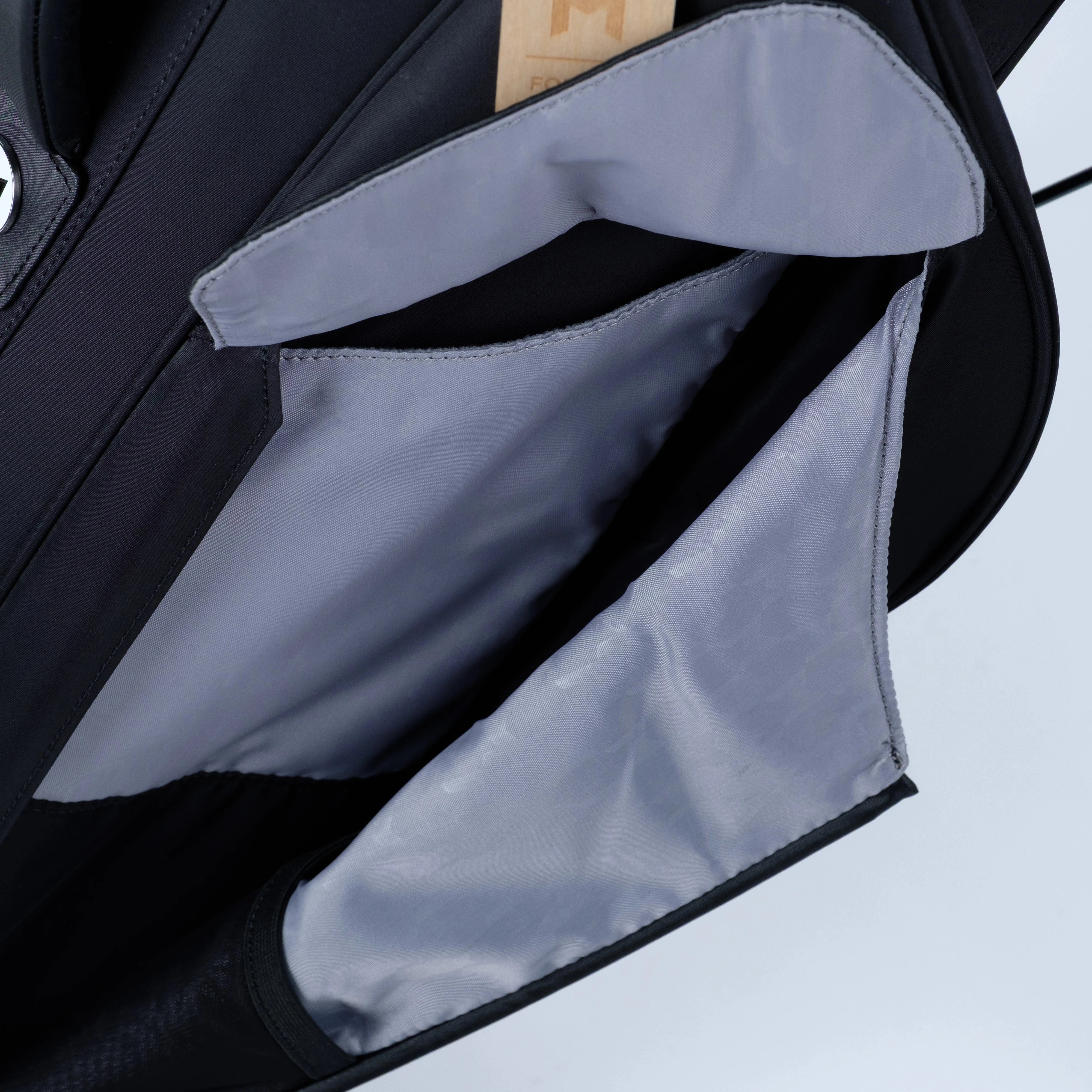 Close-up of a black bag with a gray interior pocket and a wooden tag on a light gray background.