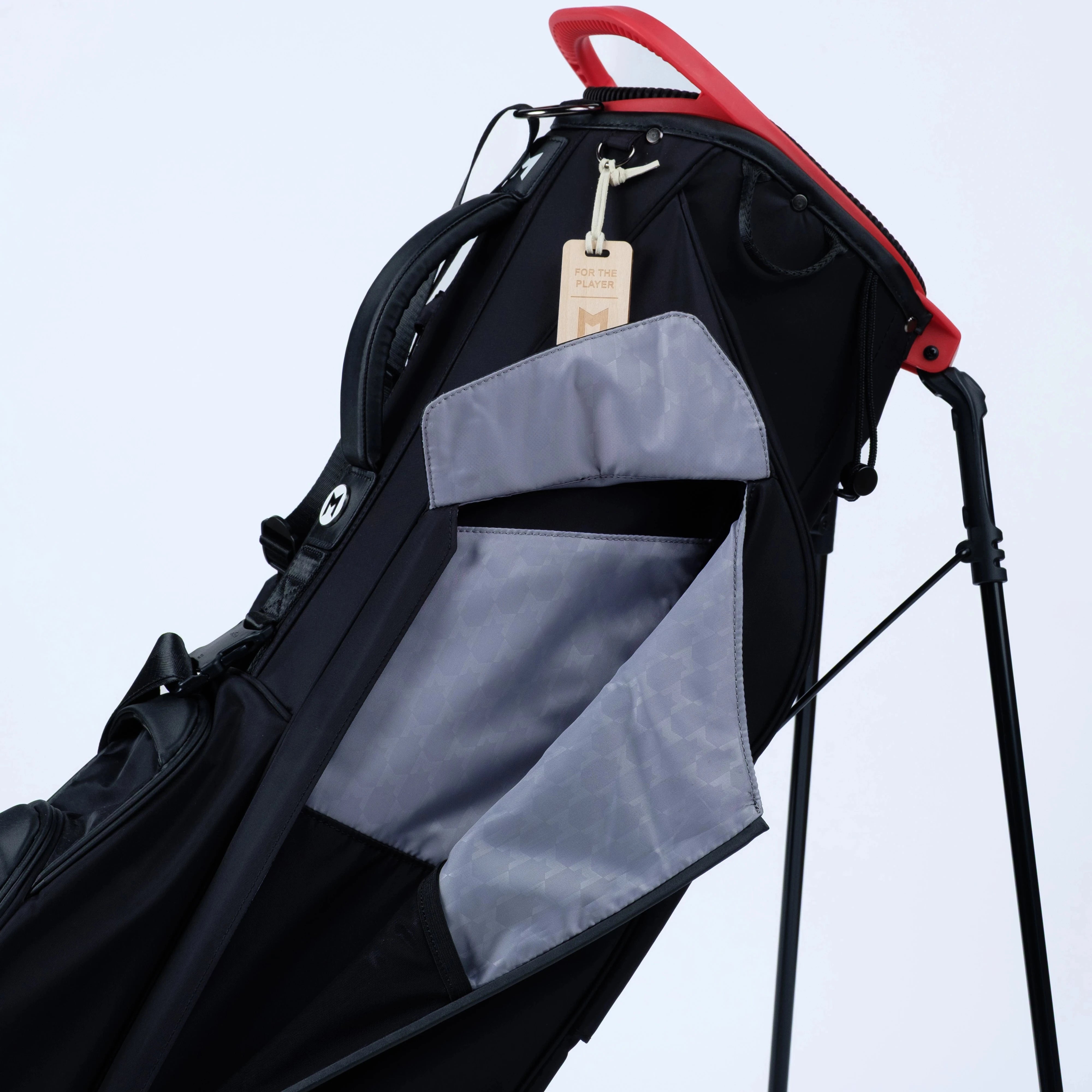 Black golf bag with gray interior and red top on a light blue background