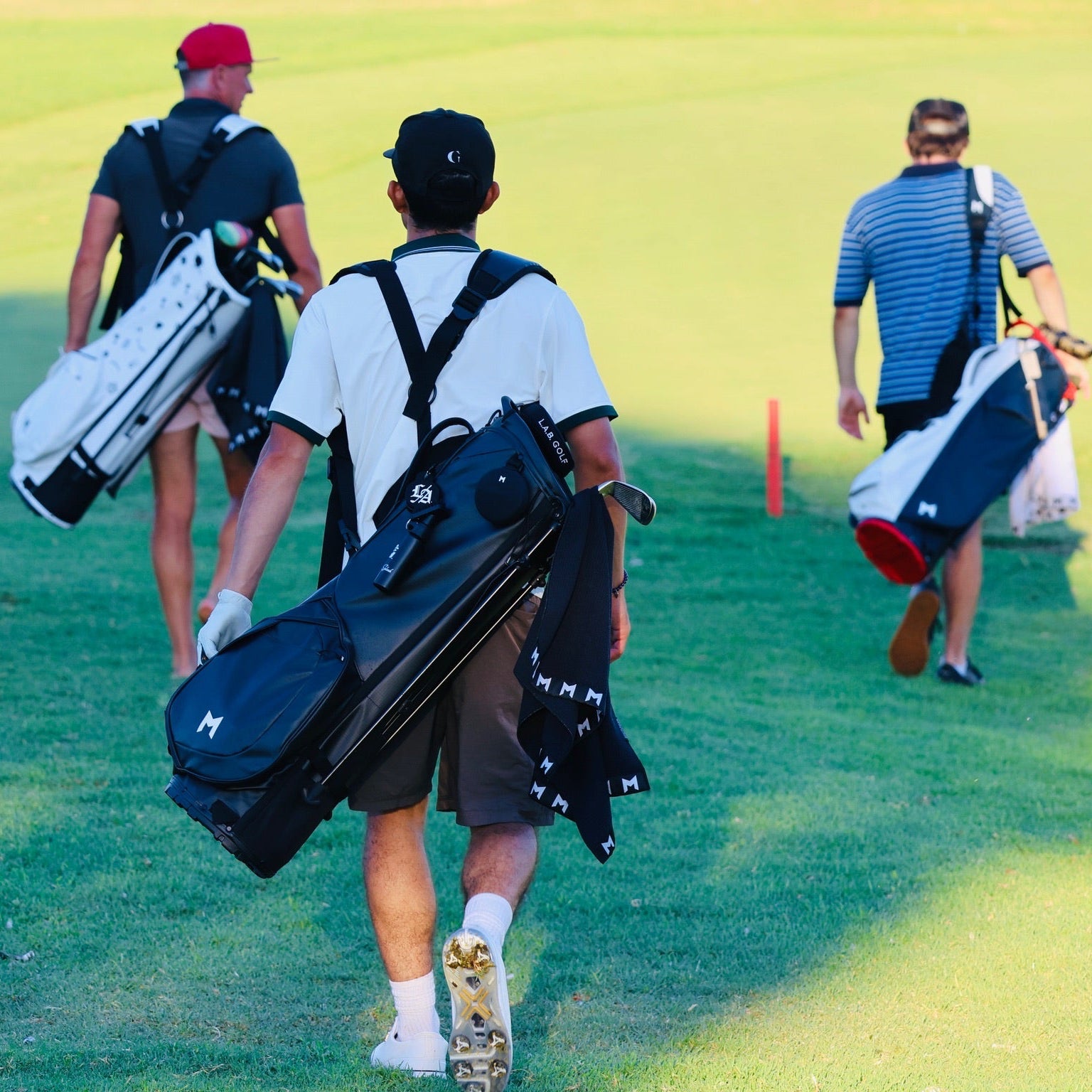 Three golfers walking on a golf course with golf bags.