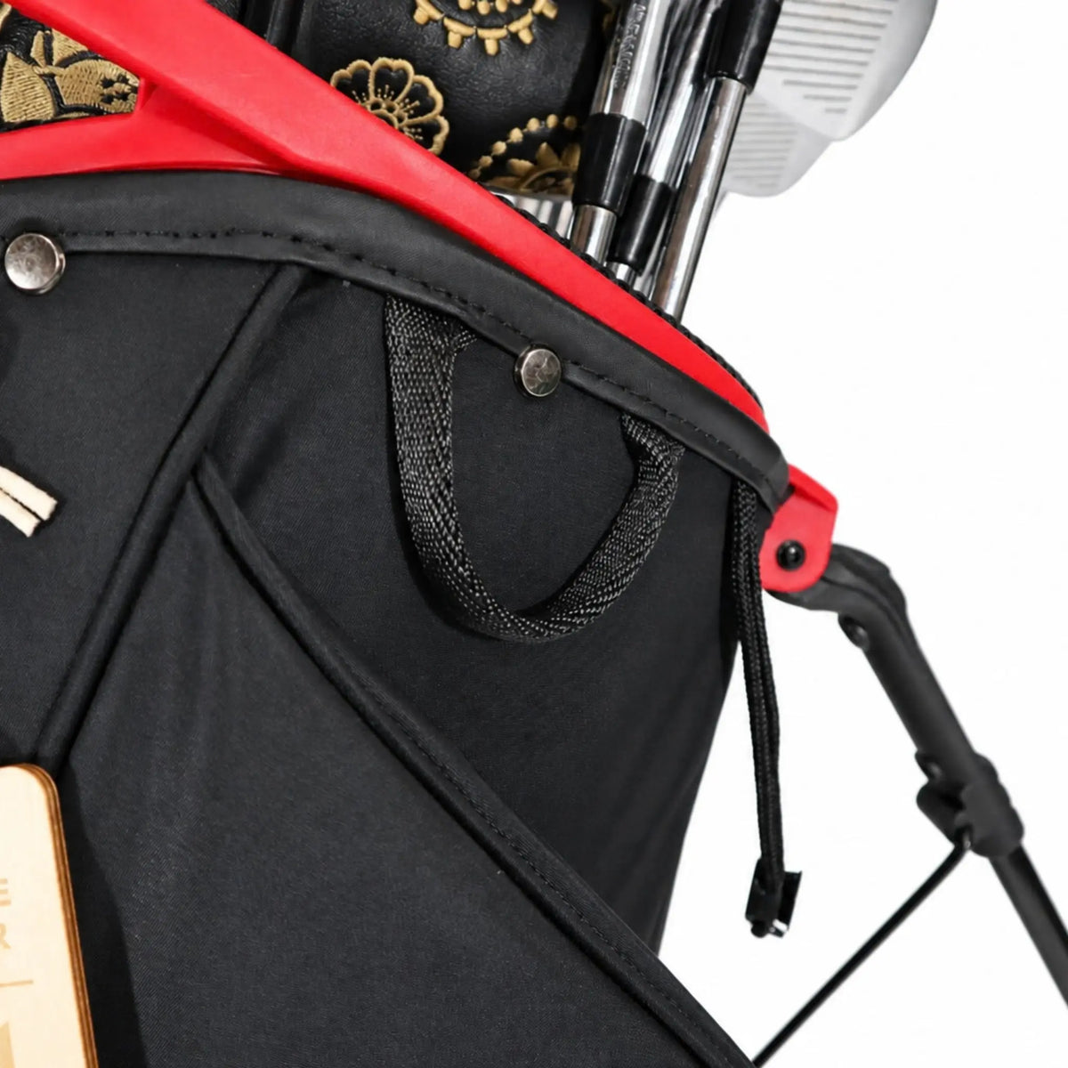 Close-up of a black golf bag with red trim, gold floral embroidery on the headcover, and golf clubs partially inserted, photographed on a white background.