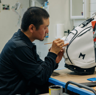 MNML GOLF's certified, lead artist Hitoshi, hand-painting a custom golf bag for a customer.