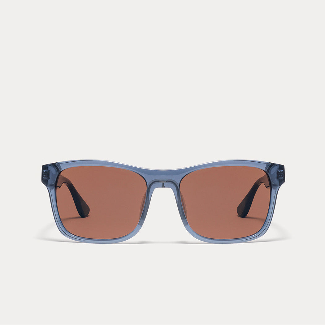 A pair of square sunglasses with translucent dusty blue frames and warm brown lenses, shown against a light gray background.