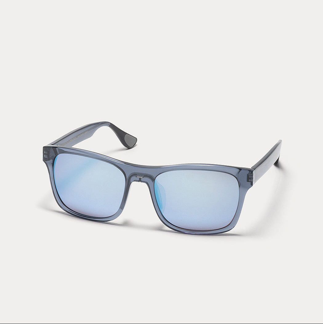 A pair of translucent smoky gray sunglasses with light blue mirrored lenses, shown at a three-quarter angle on a light gray background.