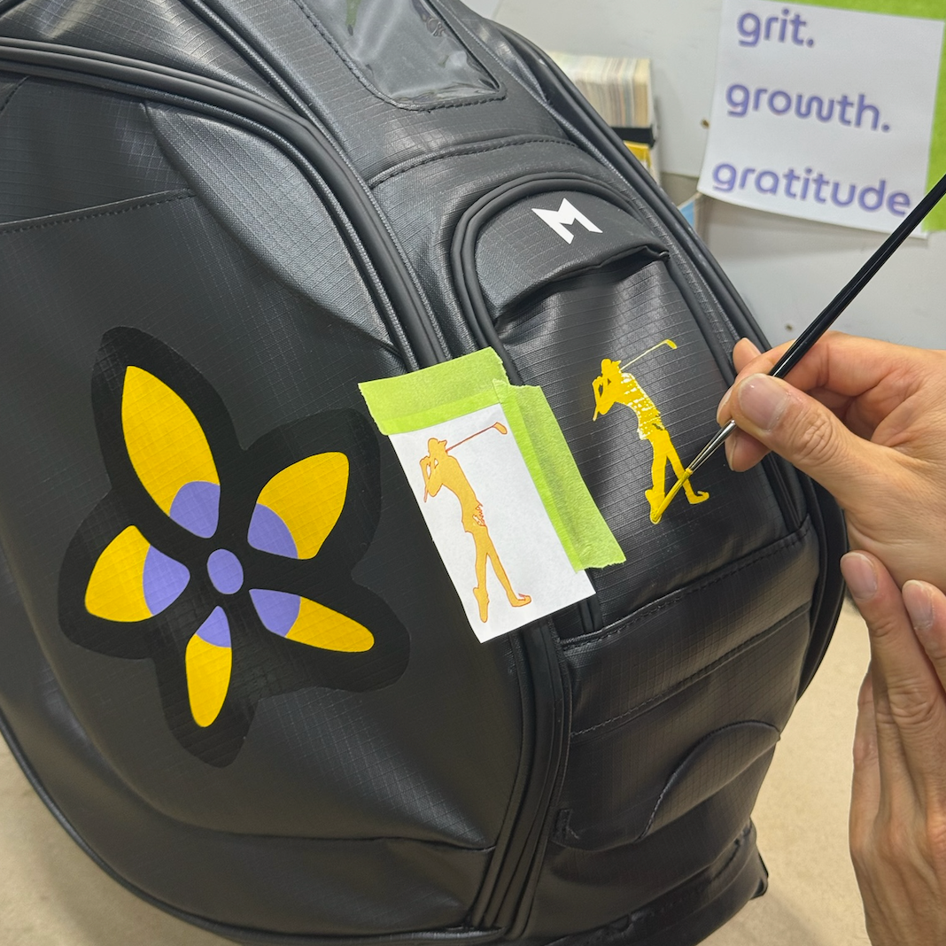 Person hand painting custom golf design on a black golf bag 
