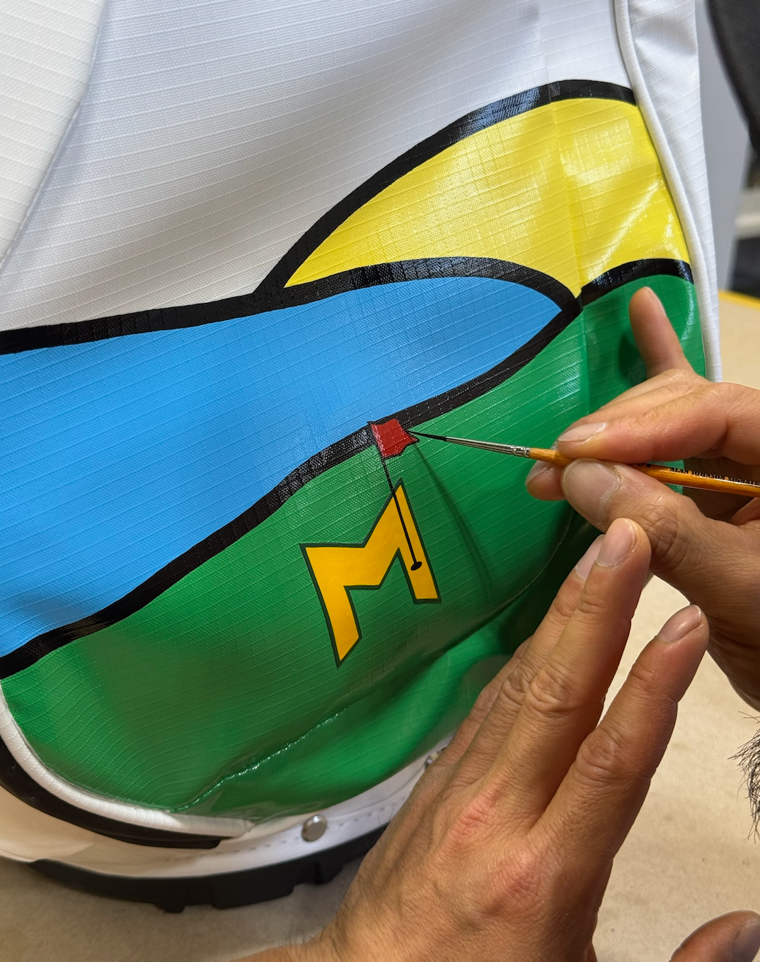 Person painting a logo on a colorful bag with a brush