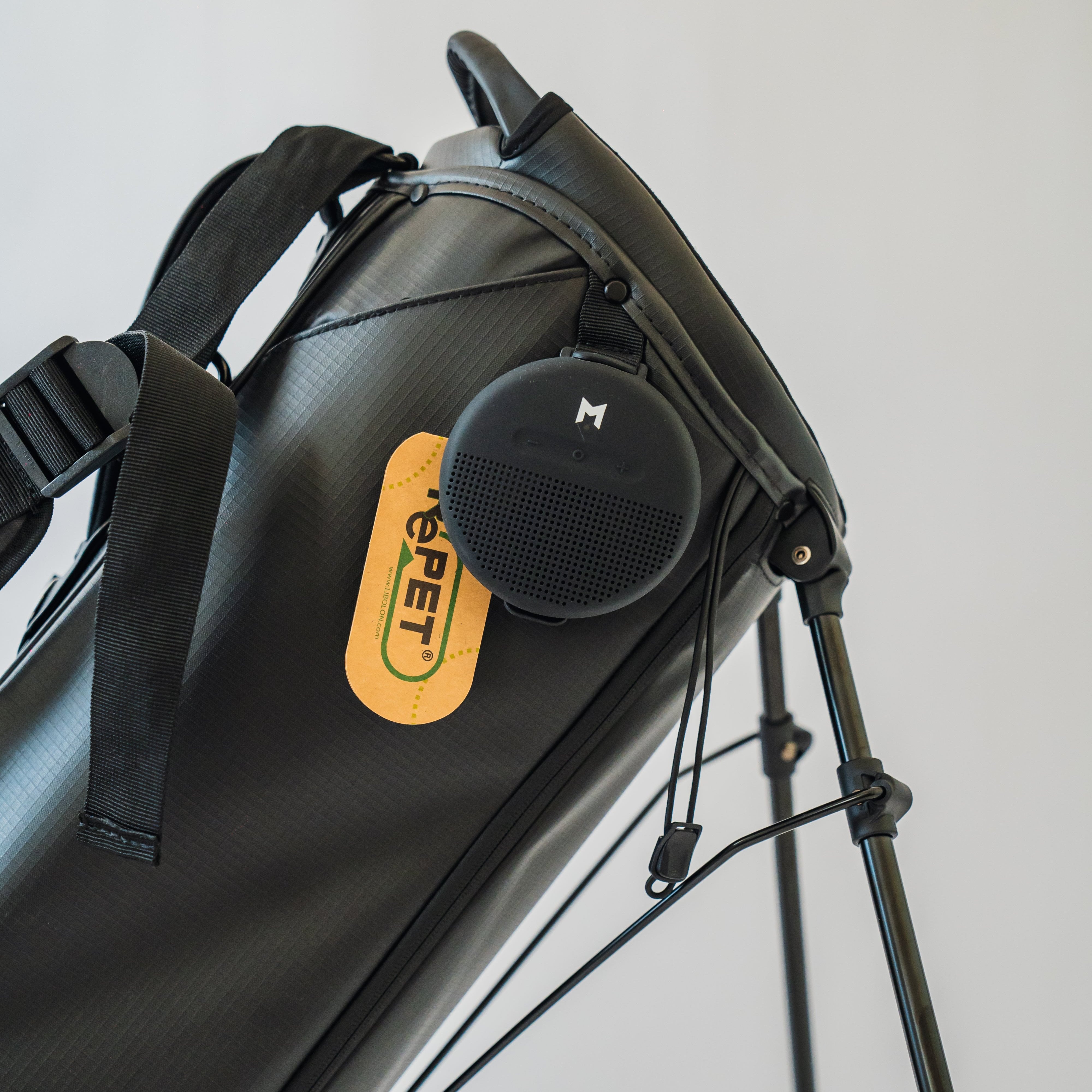 Up close bluetooth speaker with MNML GOLF's white M logo, attached to the black MR1 custom golf bag.