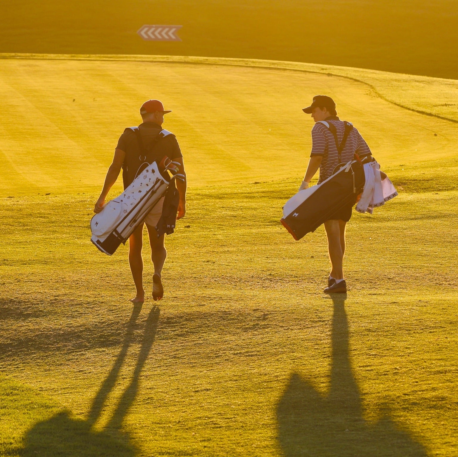Two golfers walking on a golf course with their clubs, bathed in yellow light.