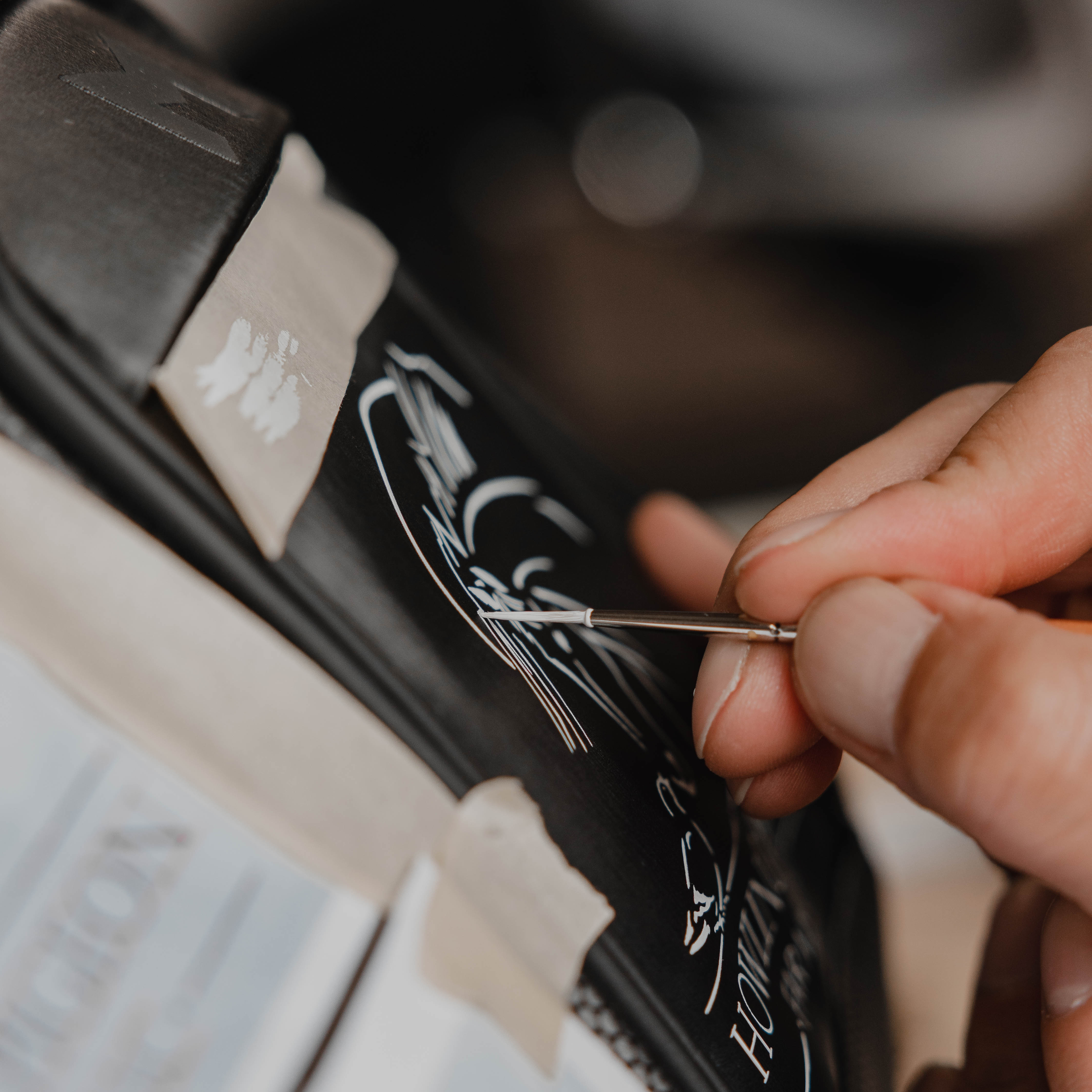 Up close of MNML GOLF's certified artists hand-painting a logo on a black MR1 custom golf bag for a customer, using a small paint brush and white paint.