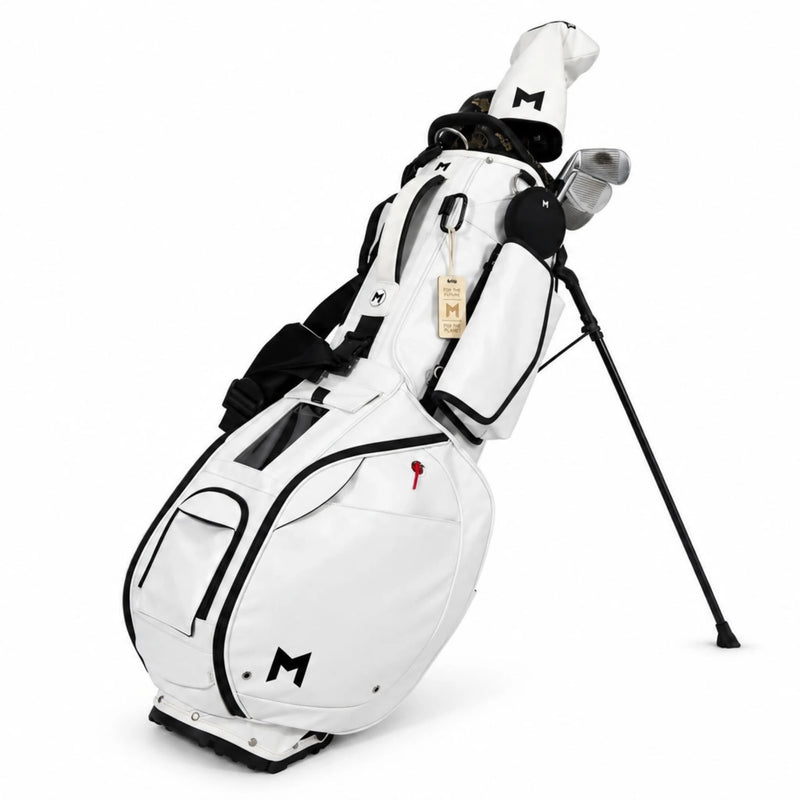 A white standbag golf bag with black trim and a black tripod leg, shown on a clean white background. The bag features multiple pockets, a top lid, and a white golf club cover with a black monogram 'M' on the front.
