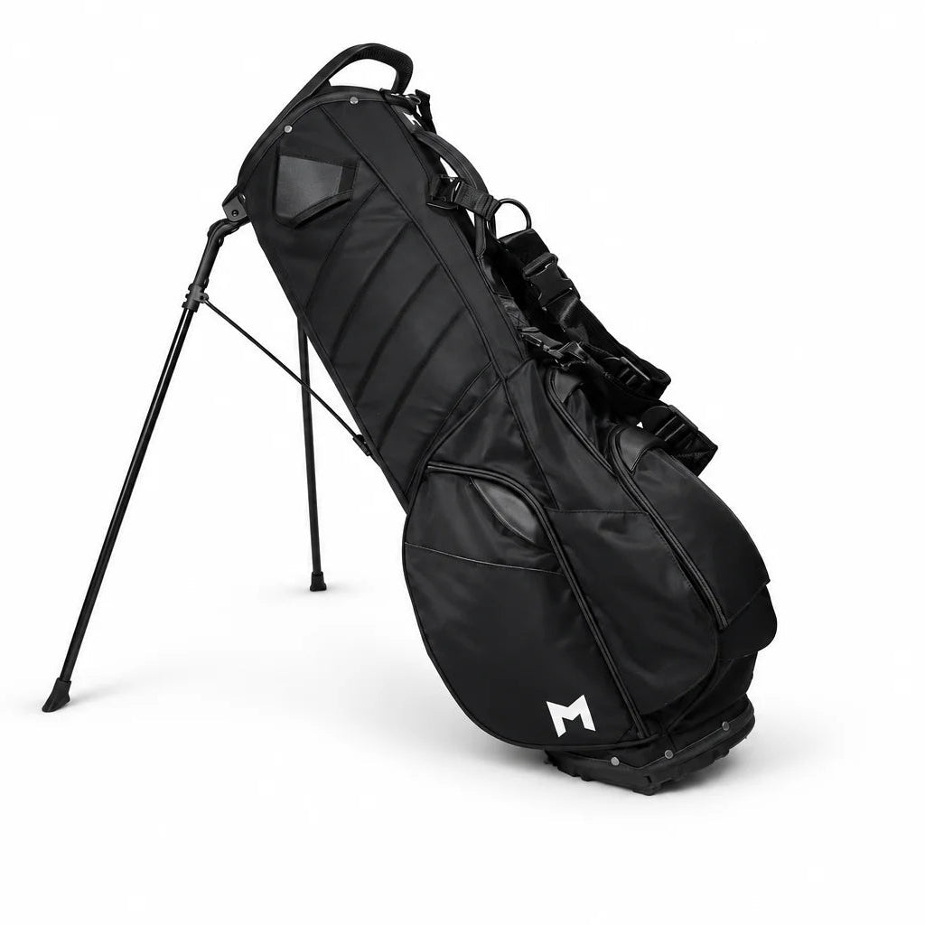 A black stand golf bag with a white stylized 'M' logo on the lower front pocket, standing on its tripod legs against a solid white background.