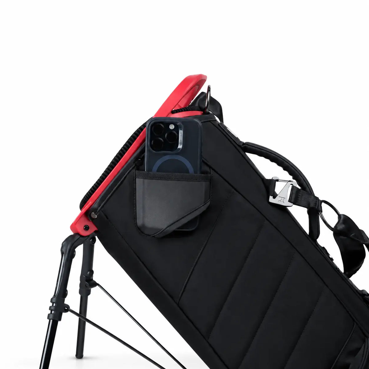 A black golf bag with a red frame accent, shown with a filming pocket and phone in its side pocket, on a clean white background.