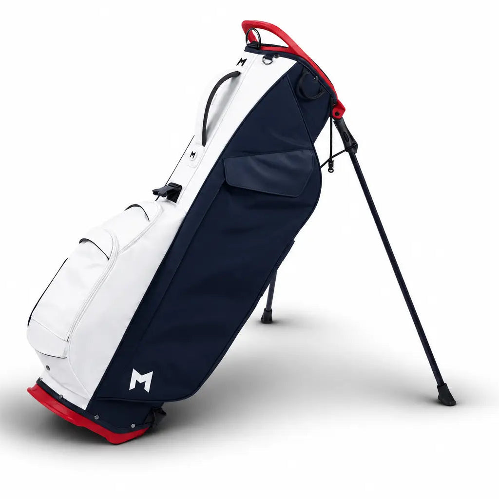 A stand-up golf bag with a navy blue and white color-blocked design, accented with red trim and a black tripod stand, shown on a white background.