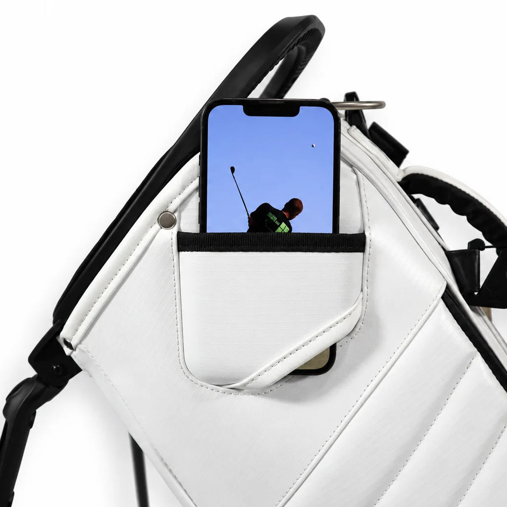 A white filming pocket on a golf bag with black trim and a side pocket holding a smartphone, shown against a plain white background.