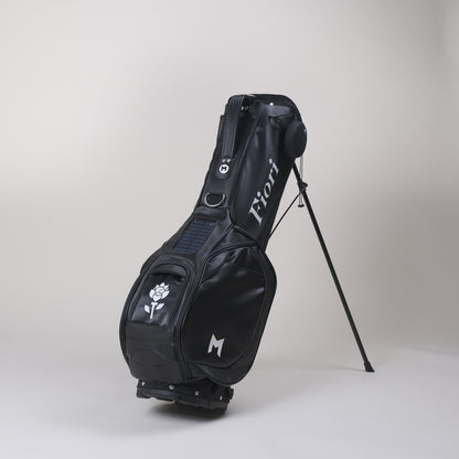Black MNML GOLF bag with custom, hand painted Fiori flower logo and MNML GOLF M logo. Solar power phone charger and ball marker attached and magnetic ball pocket displayed.